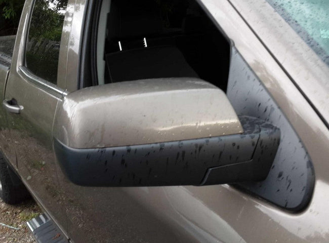 A close-up of a dusty beige pickup truck's side mirror 
